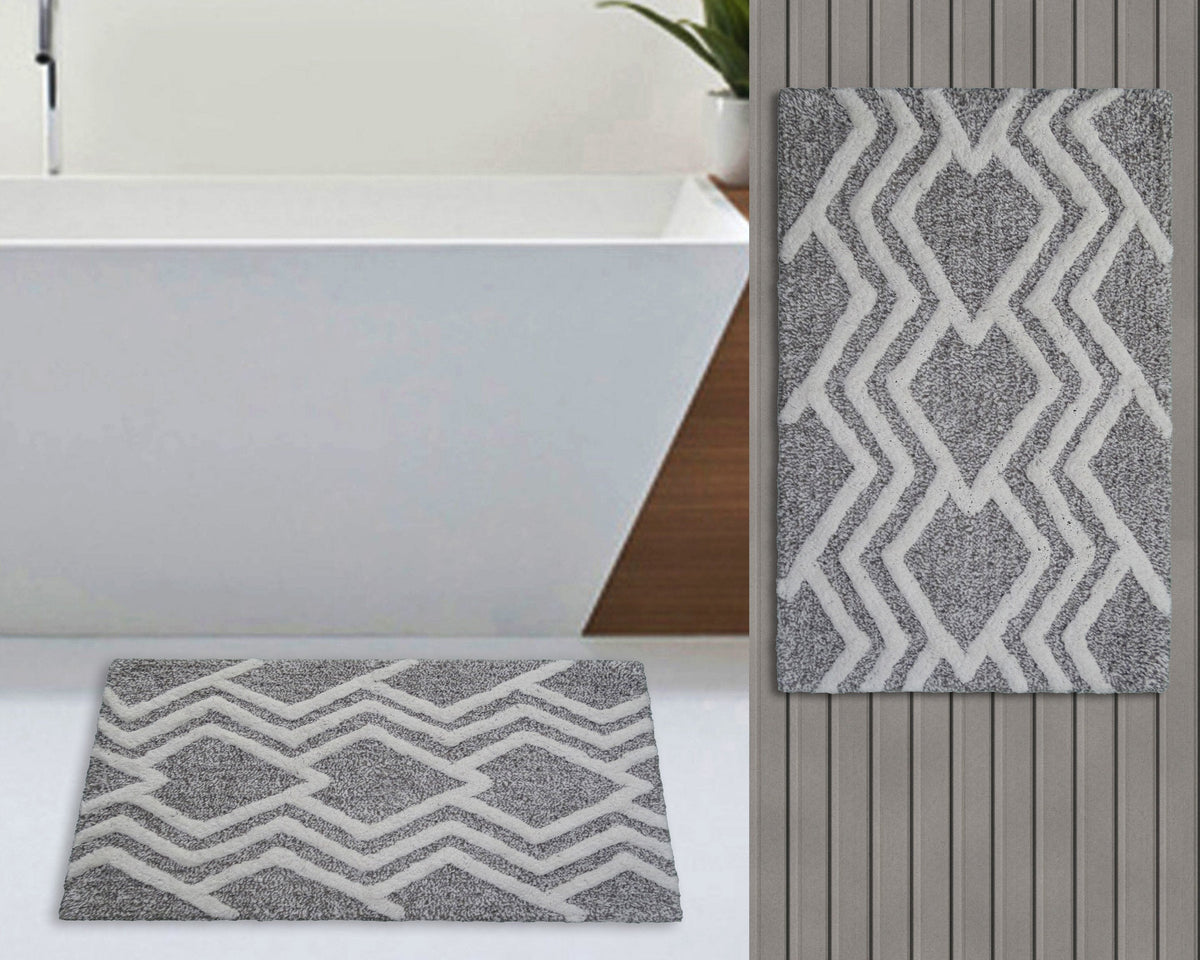 Rectangular bath rug with a grey background and ivory geometric zigzag diamond pattern, shown laid flat and hanging vertically in a bathroom setting.