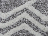Close-up of a textured bath rug featuring an ivory zigzag geometric pattern on a grey background with a soft, plush surface.