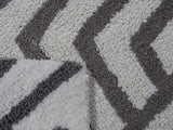 Close-up of a looped bath rug showing a grey and ivory geometric chevron pattern with a folded corner revealing the backing.