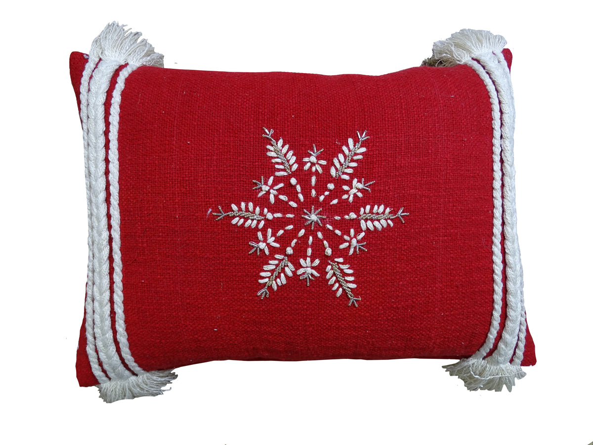 Rectangular red throw pillow with white embroidered snowflake centered, featuring braided white tassels on all four corners against a white background.