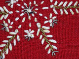 Close-up of red woven fabric with white and gold embroidered floral and leaf patterns accented by small silver bead clusters.