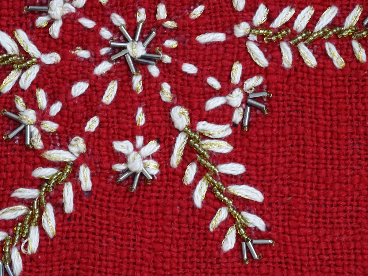 Close-up of red woven fabric with white and gold embroidered floral and leaf patterns accented by small silver bead clusters.