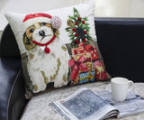 White throw pillow featuring a dog wearing a red Santa hat next to a stack of colorful wrapped Christmas gifts with a small festive tree on top, displayed on a sofa.
