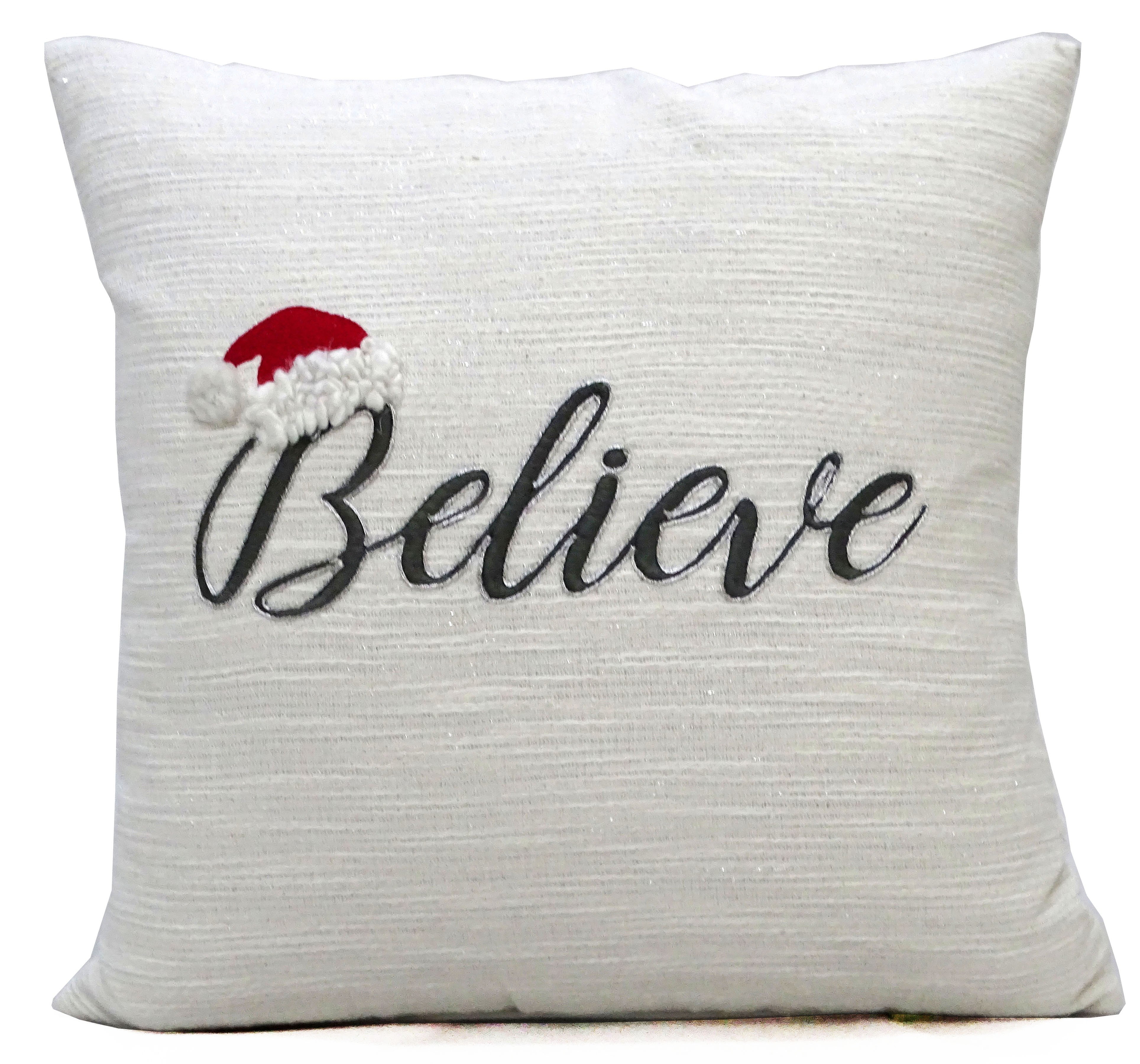 White 20 by 20 inch Vibhsa Christmas pillow with embroidered Santa cap and Believe text on a couch