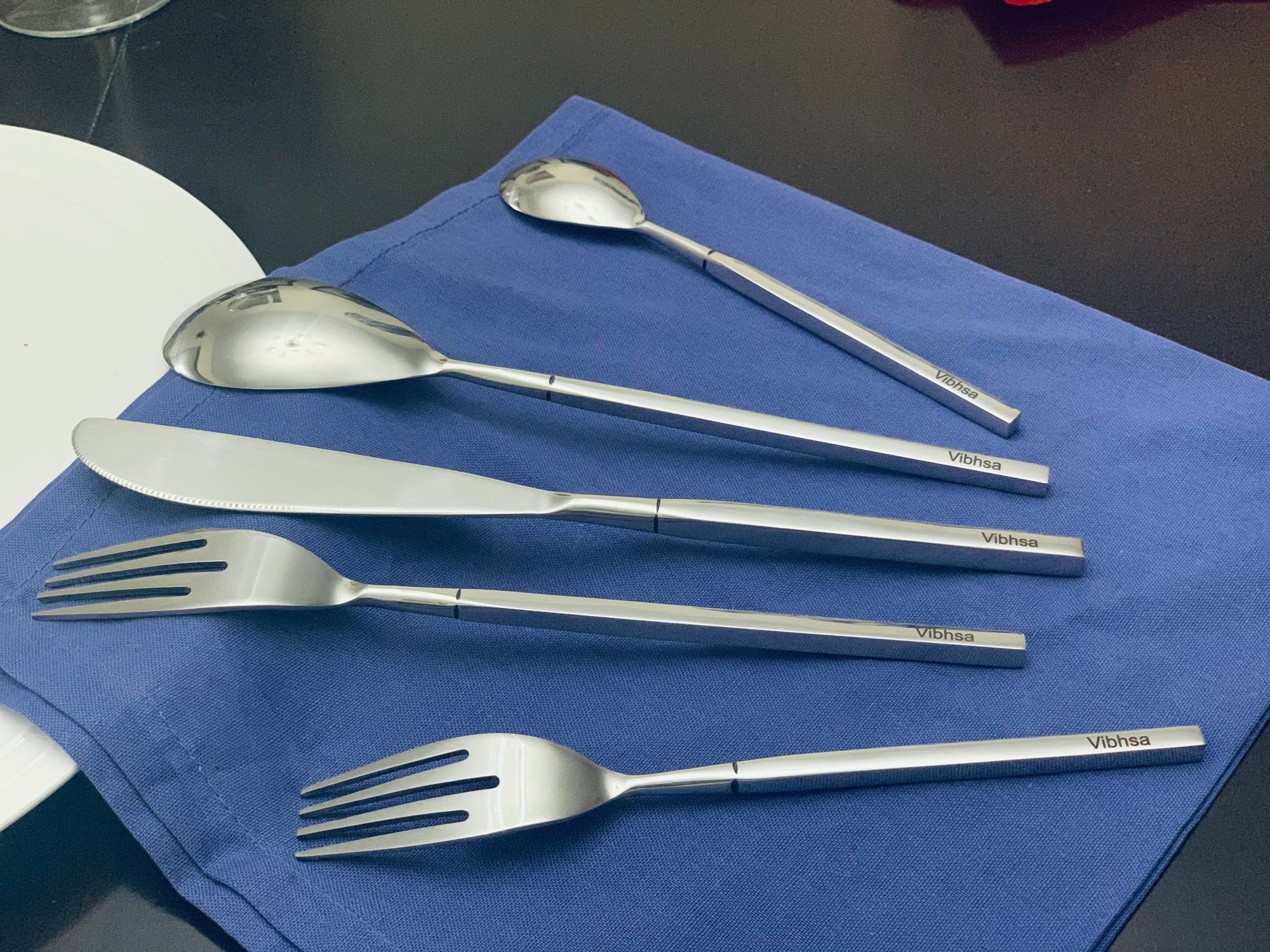 Vibhsa Modern Stainless Steel Flatware Set arranged on a wooden table, showing forks, knives, and spoons with a reflective surface
