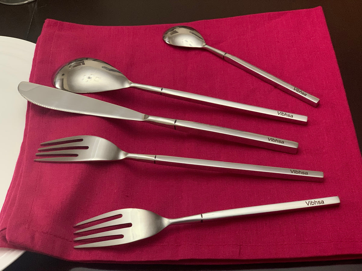 Five pieces of modern stainless steel flatware including two forks, two spoons, and one knife, arranged on a folded deep pink cloth with branded handles.