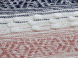 Close-up of a woven textile showing white textured dots over navy blue and white thread, and a dusty pink and white geometric pattern below.