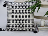 Black and white woven throw pillow with tassels placed on a fabric couch