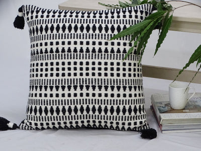 Black and white woven throw pillow with tassels placed on a fabric couch