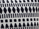 Close-up of a black and white woven throw pillow featuring geometric patterns including rows of diamonds, dots, and pyramid shapes on a textured fabric.