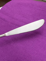 Silver serrated butter knife with a smooth handle resting on a purple fabric background.