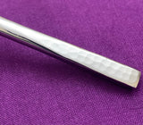 Close-up of a silver flatware handle with a hammered texture against a purple fabric background, highlighting the subtle dimples and smooth polish.