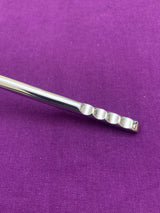 Close-up of a shiny silver flatware handle with a unique indent pattern on a purple fabric background.