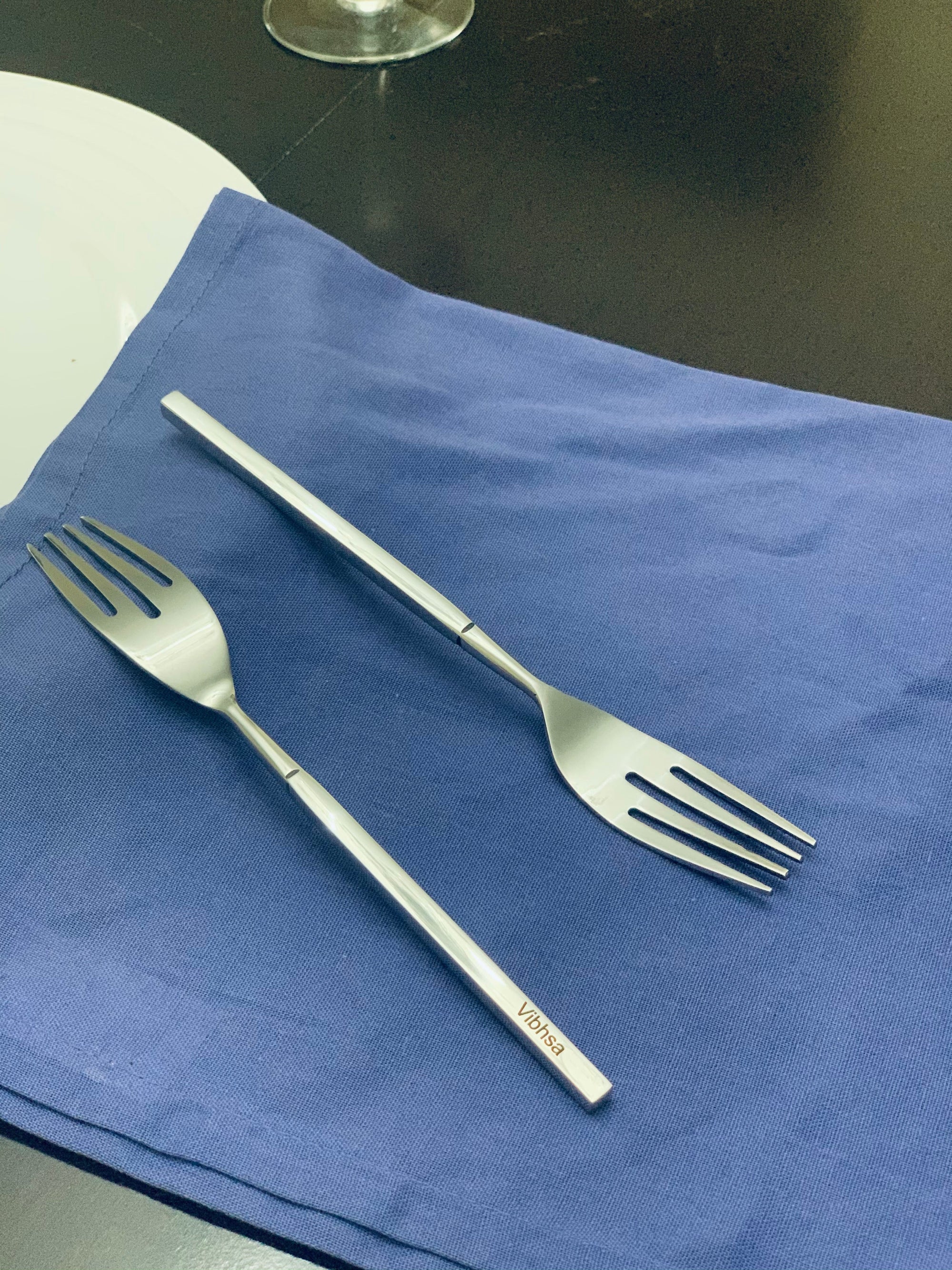 Set of six Vibhsa polished stainless steel salad forks displayed on textured gray fabric