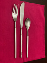 Stainless steel flatware set including a dinner fork, serrated dinner knife, and dessert spoon with straight handles, arranged on a red cloth.