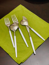 Set of stainless steel flatware with white handles including two forks, two spoons, and one butter knife displayed on a green cloth against a dark surface.