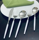 White and silver stainless steel flatware set with hammered mouth detailing laid out on dark surface