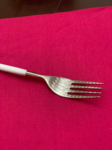 Fork with a white handle and a hammered stainless steel head resting on a bright pink fabric surface