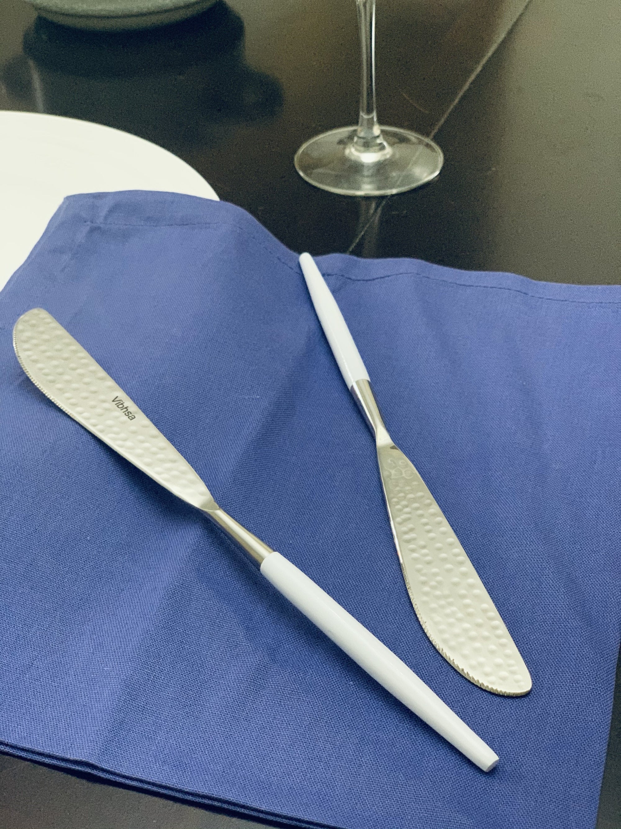 Six white-handled dinner knives arranged with hammered stainless steel blades visible