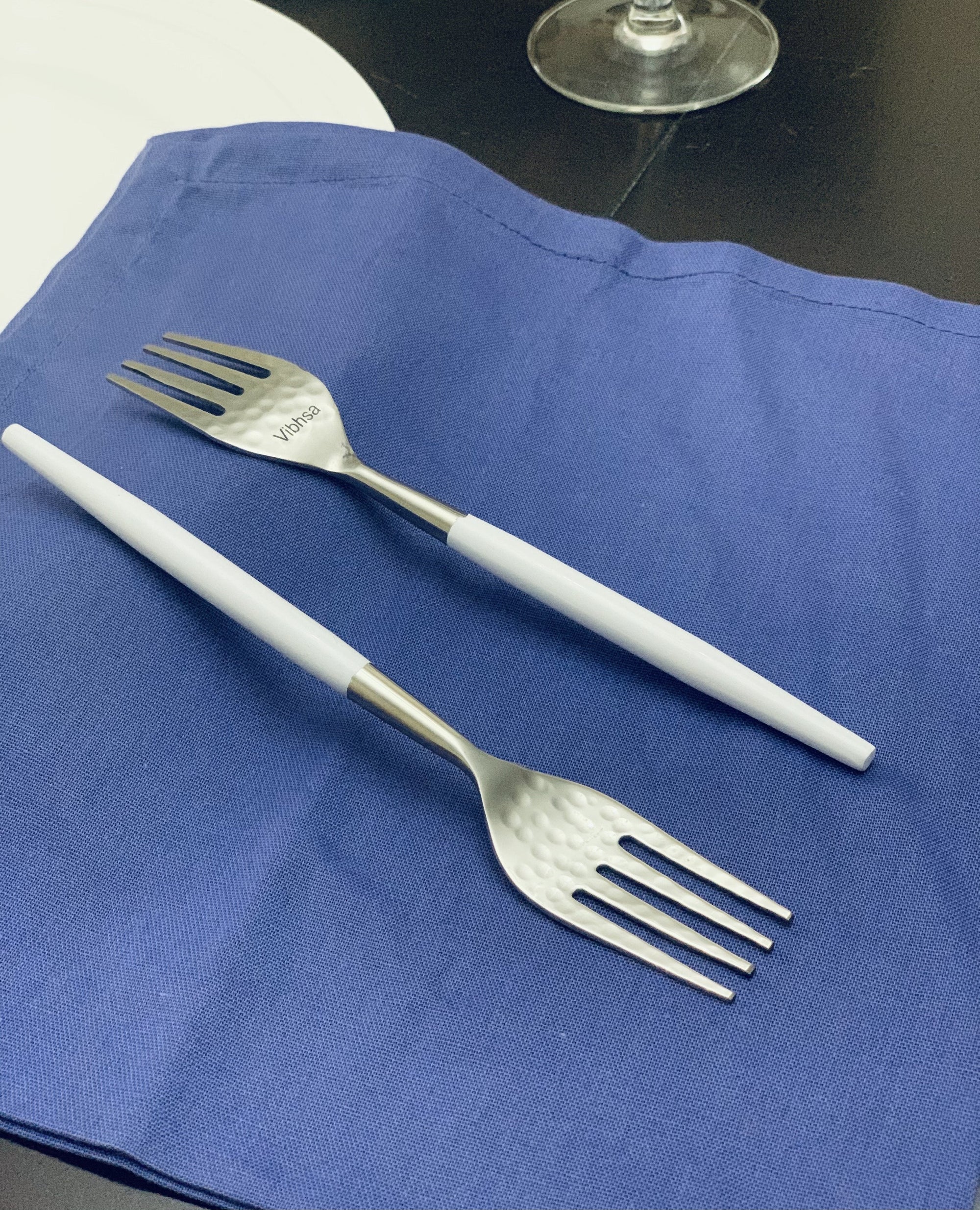 Set of six 7-inch salad forks with hammered mouth and white handles arranged on a surface