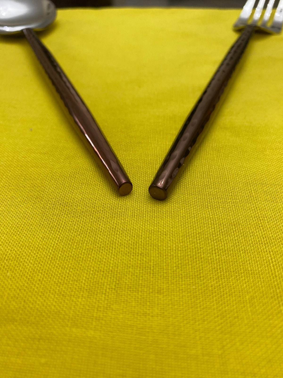 Close-up of brown hammered stainless steel knife and fork handles resting on bright yellow fabric, showing textured and smooth finishes.