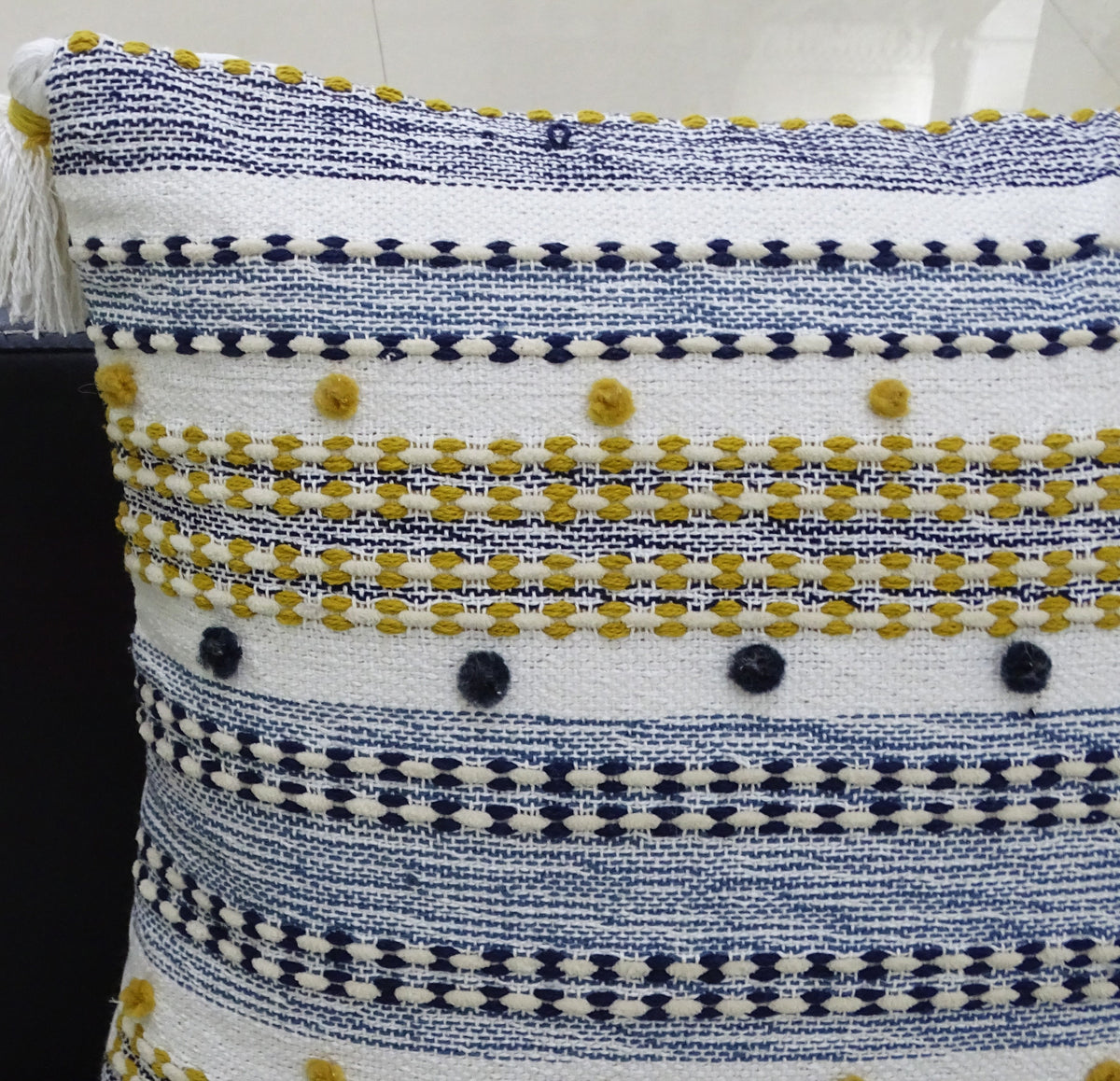 Rectangular pillow with alternating navy blue and mustard yellow striped patterns, featuring small pom details and a white tassel on one corner.