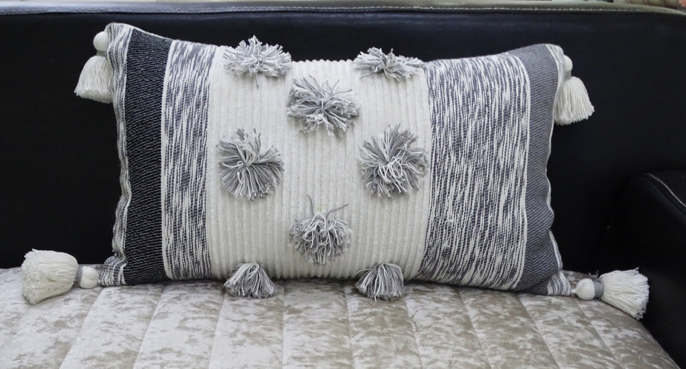 Melange striped throw pillow with large pom-poms and tassels on a sofa