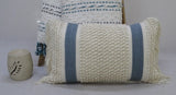 Rectangular decorative pillow with cream loop texture and two vertical blue stripes, featuring fringe on both ends, displayed in front of a folded textile with blue accents and a carved stone candle holder.