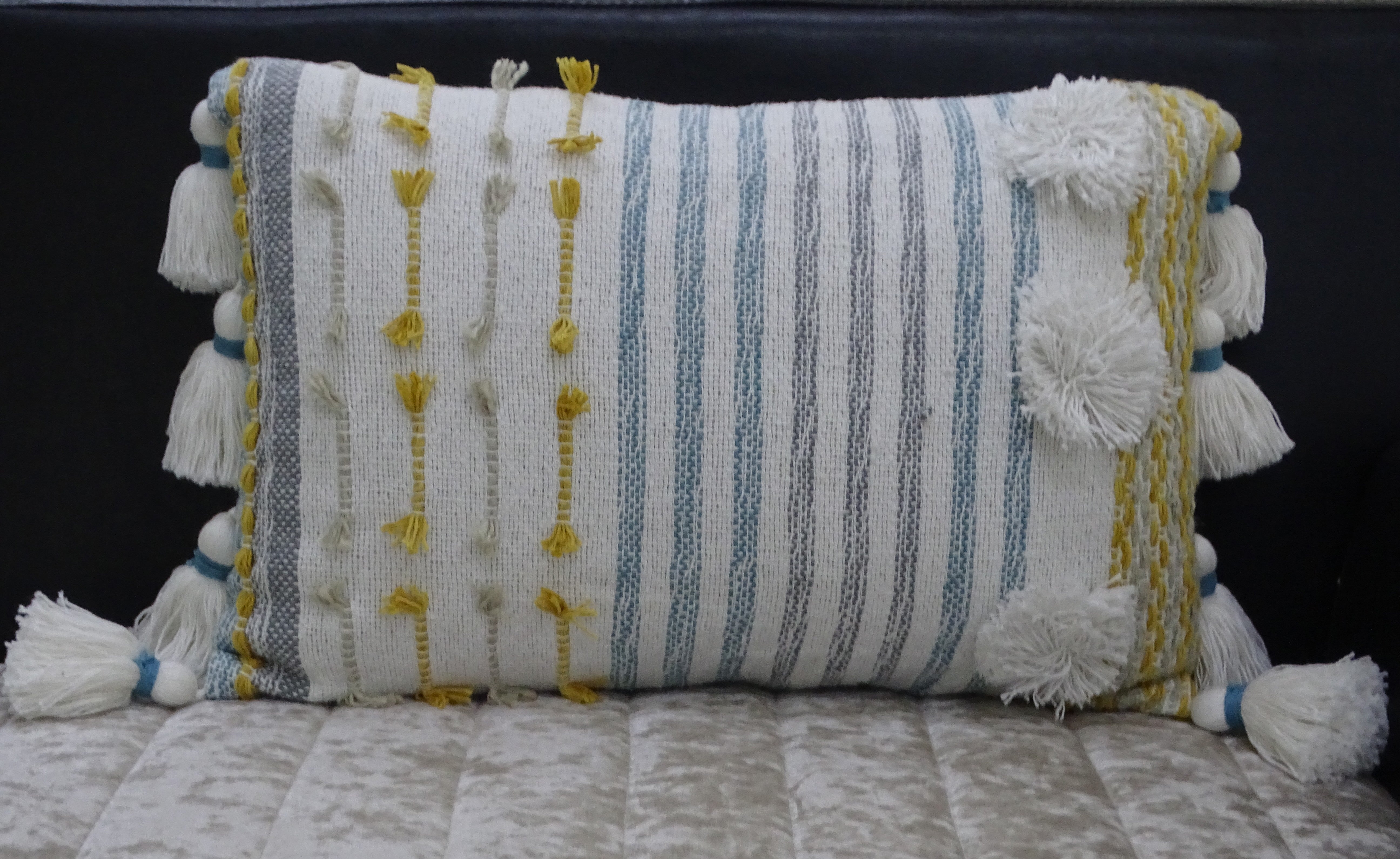 Designer striped throw pillow with large poms and tassels displayed on a sofa