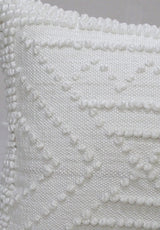 Close-up of white 18x18 inch outdoor pillow with textured geometric pattern of raised dots and lines on woven fabric surface.