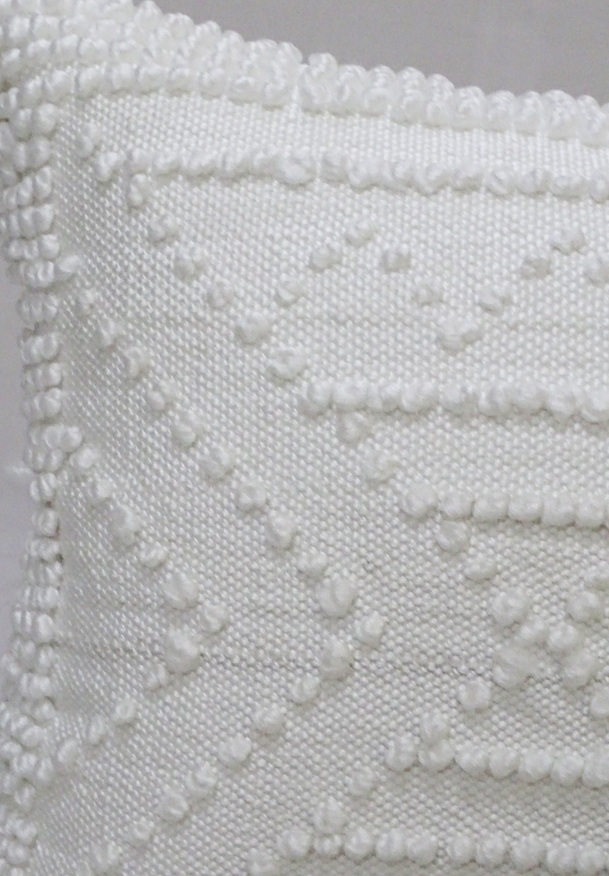 Close-up of white 18x18 inch outdoor pillow with textured geometric pattern of raised dots and lines on woven fabric surface.