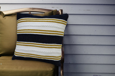 Multi Color 18x18 inch indoor outdoor pillow with braid detail resting on a sofa