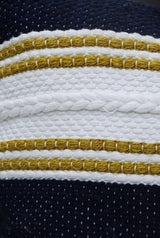 Close-up of a woven pillow with a textured white braid and mustard yellow stripes on a navy blue background.