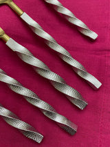 Close-up of five twisted stainless steel flatware handles with textured pattern, attached to golden tops, arranged diagonally on a deep red fabric background.