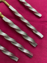Close-up of five golden stainless steel flatware handles with twisted, textured silver grips arranged diagonally on a magenta fabric background.