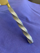 Close-up of a twisted, textured stainless steel flatware handle with a smooth golden top, set against a purple fabric background.