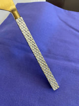 Close-up of a flatware handle featuring a textured silver pattern and a smooth golden blade against a blue fabric background.