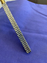 Close-up of a textured stainless steel knife blade with a honeycomb pattern, resting on a blue fabric background, with a glimpse of a gold-colored handle.