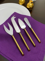 Set of four golden-handled cheese knives with stainless steel blades arranged on a flat surface