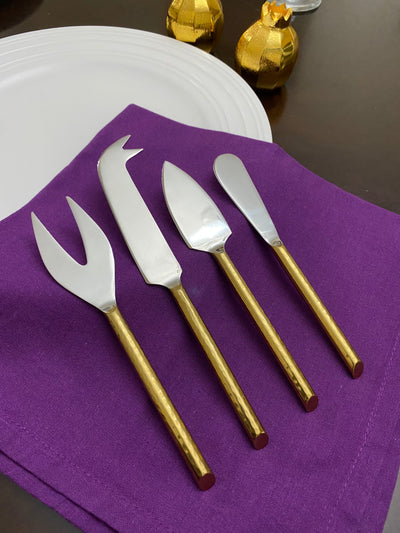 Set of four golden-handled cheese knives with stainless steel blades arranged on a flat surface