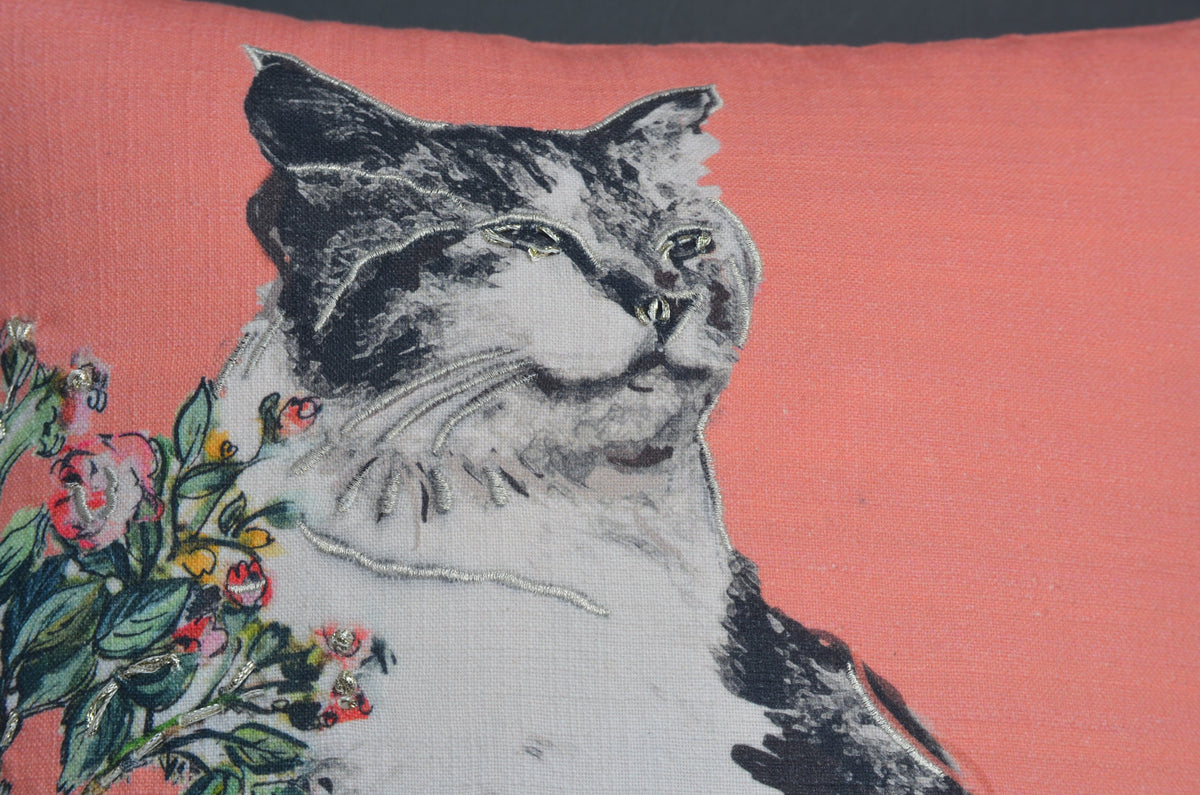 Close-up of a pink decorative pillow featuring a printed black and white cat with flowers on the left side.