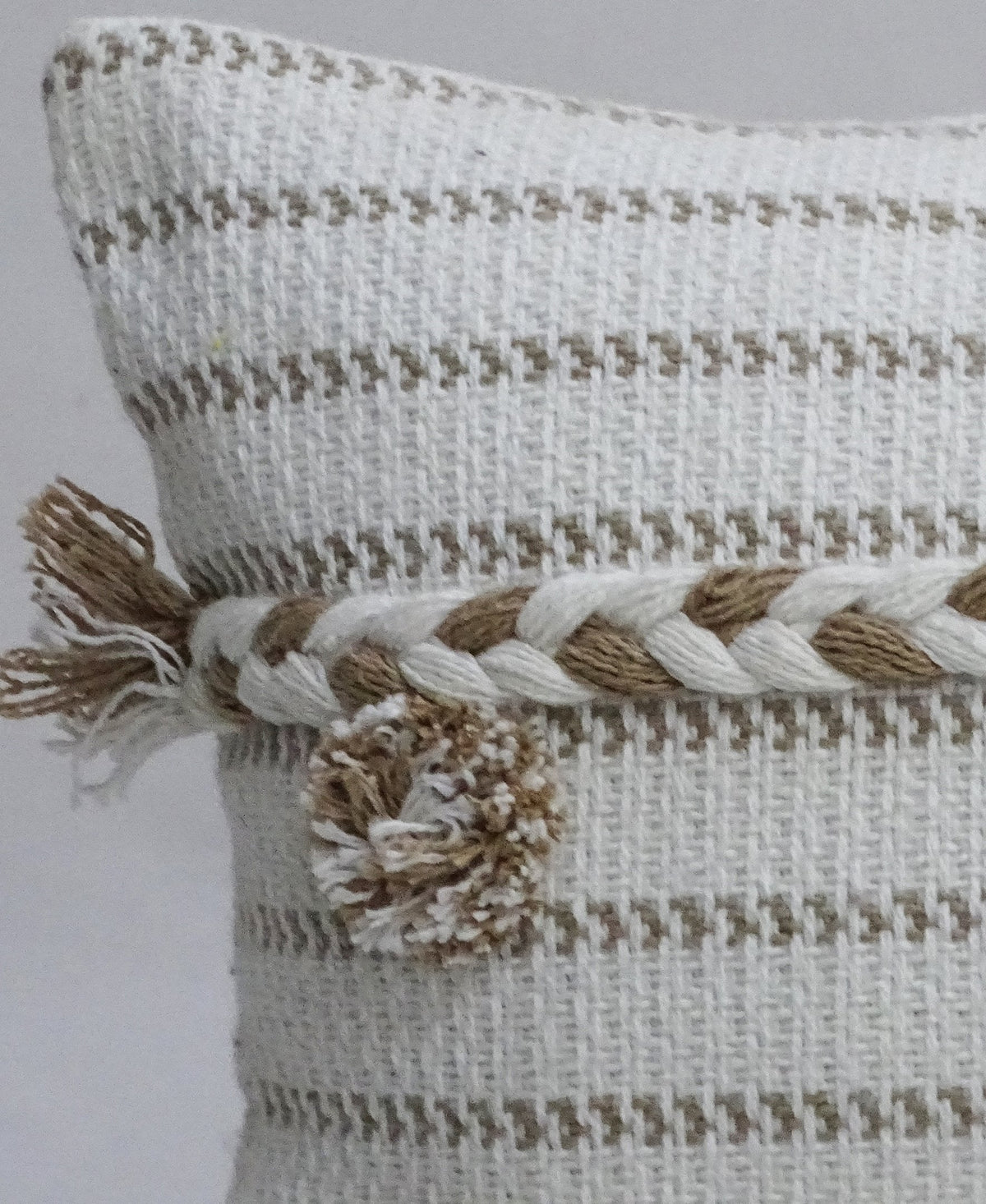 Close-up of a handwoven 14x24-inch throw pillow featuring beige and white horizontal stripes, a twisted rope detail, and a textured pom pom on the corner.