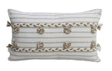 Rectangular off-white throw pillow with horizontal beige stripes, decorated with evenly spaced beige poms and tassels along edges on a white background.