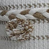 Close-up of a beige and white woven fabric with a braided detail and a small, textured pom-pom in natural tones.