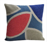 Square throw pillow with abstract embroidery pattern in red, blue, gray, and beige shapes on a blue background, showing textured yarn details.