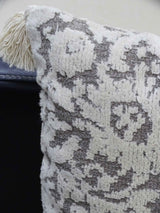 Close-up of a textured throw pillow with cream tassels and an abstract cream and gray woven pattern on fabric.