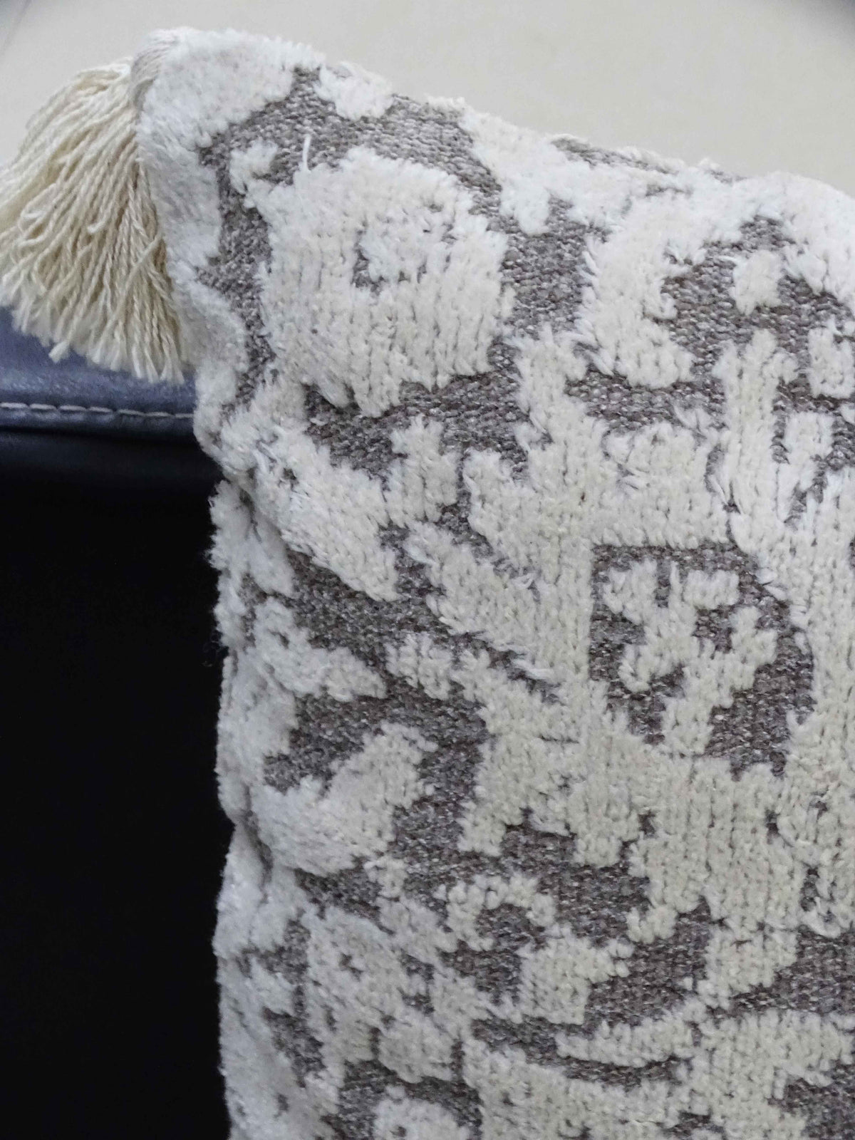 Close-up of a textured throw pillow with cream tassels and an abstract cream and gray woven pattern on fabric.
