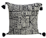 Square beige throw pillow with a black geometric Aztec-inspired pattern and black tassels on each corner.