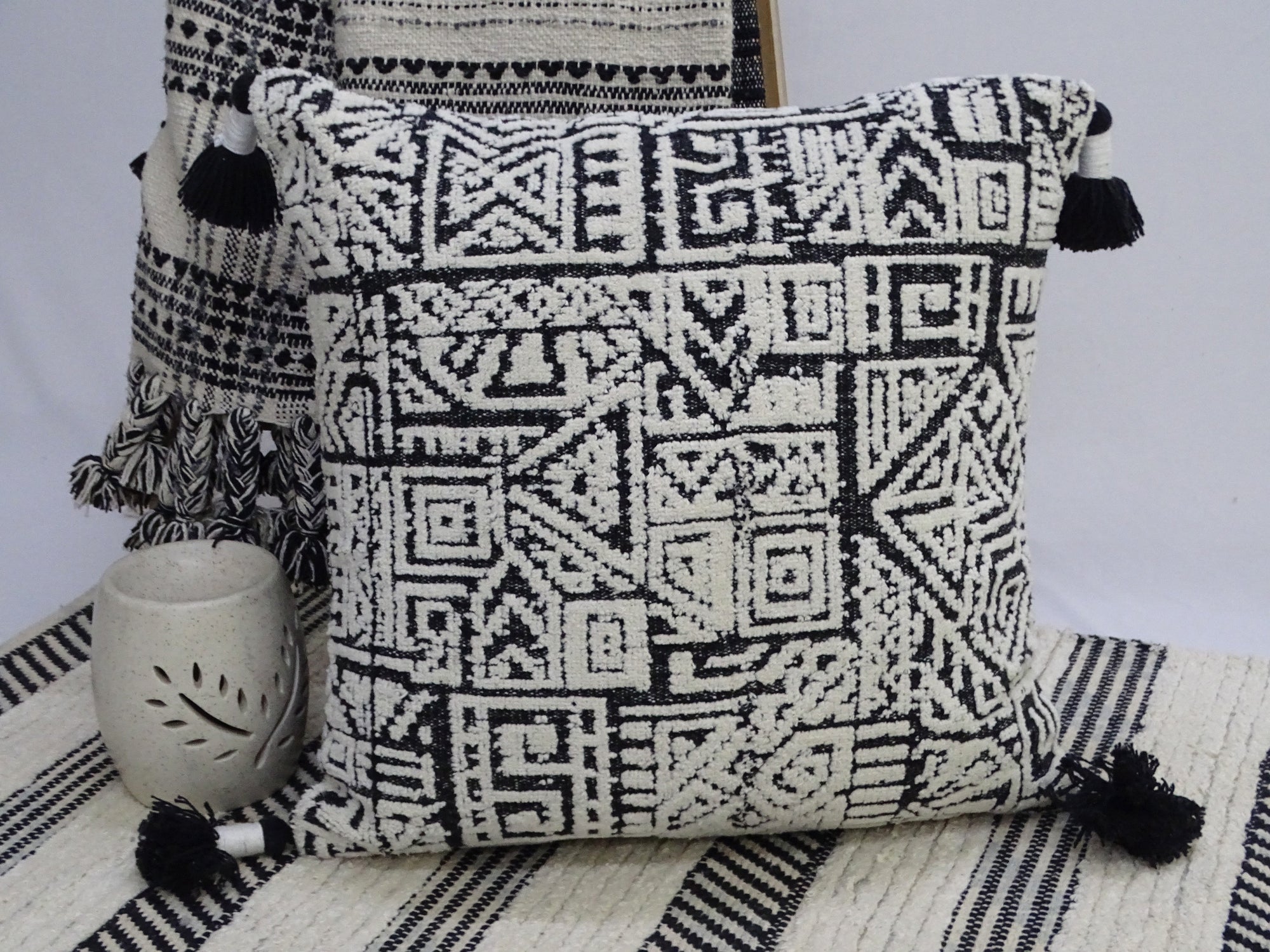 Colorful 20 by 20 inch throw pillow with corner tassels on a neutral surface