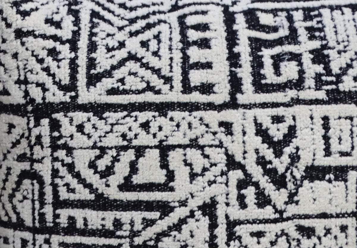 Close-up of a black and white textile with a geometric, tribal-inspired pattern composed of squares and angular lines.